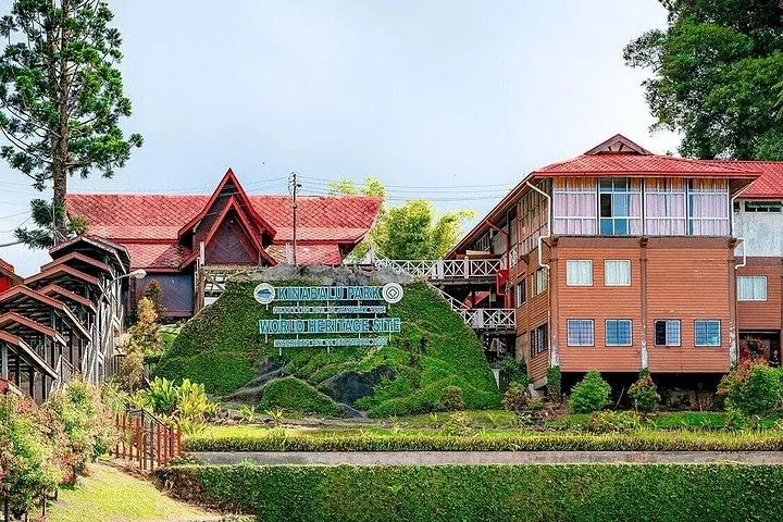 Cartel de entrada al sitio del Patrimonio Mundial del Parque Kinabalu con edificios tradicionales detrás