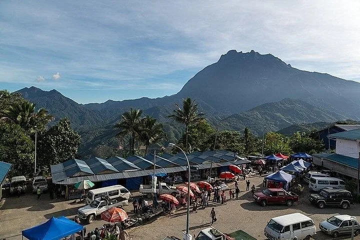 Concurrido mercado al aire libre con el Monte Kinabalu al fondo bajo un cielo azul