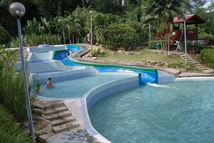 Piscina al aire libre con un tobogán azul sinuoso rodeada de plantas tropicales